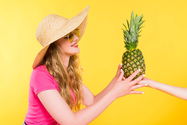 beautiful girl in Straw Hat giving pineapple to woman Isolated On yellow  - Photo, Image