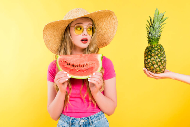 beautiful surprised girl in Straw Hat with watermelon looking at pineapple On yellow  - Fotó, kép