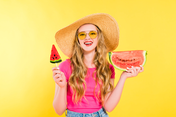 όμορφη χαμογελαστή κορίτσι σε ψάθινο καπέλο με καρπούζι και γλειφιτζούρι στο κίτρινο - Φωτογραφία, εικόνα
