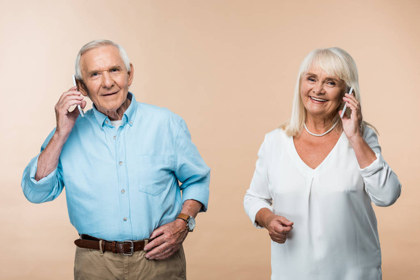 Gelukkig gepensioneerd paar met grijs haar praten over smartphones geïsoleerd op beige  - Foto, afbeelding