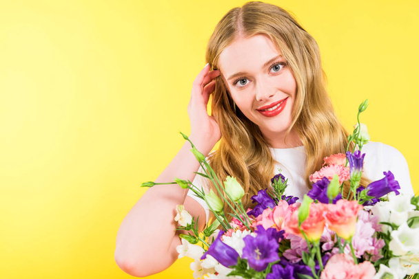 beautiful smiling blonde girl with flowers touching hair On yellow - Fotoğraf, Görsel