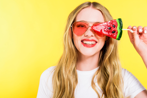beautiful happy girl in sunglasses with lollipop in shape of watermelon Isolated On yellow  - Foto, afbeelding