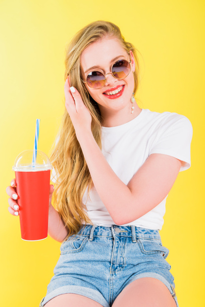 beautiful happy girl in sunglasses with drink in disposable cup Isolated On yellow  - 写真・画像