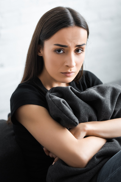upset young woman hugging pillow and looking at camera while suffering from depression at home - Valokuva, kuva