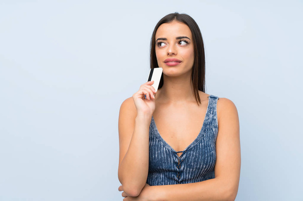 Young woman over isolated blue wall holding a credit card - Fotografie, Obrázek