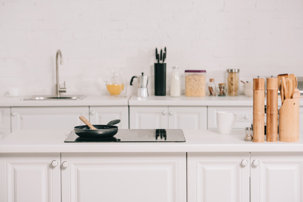 Beyaz mobilya ve pişirme yüzeyinde tava ile geniş mutfak - Fotoğraf, Görsel