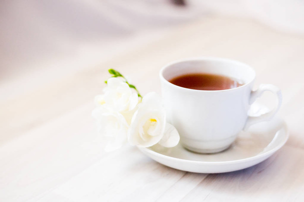 受け皿に紅茶を入れ、白いフリージアの花を - 写真・画像