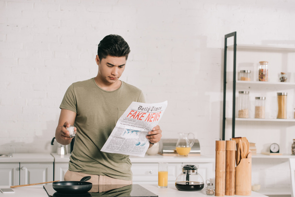 handsome asian man preparing breakfast while reading fake news newspaper in kitchen - Foto, imagen