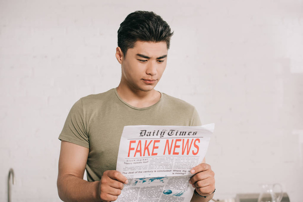 young, attentive asian man reading fake news newspaper in kitchen  - Fotografie, Obrázek