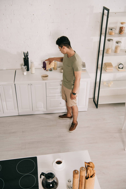 високий кут зору молодий чоловік додає пластівці в миску, стоячи біля кухонного столу
 - Фото, зображення