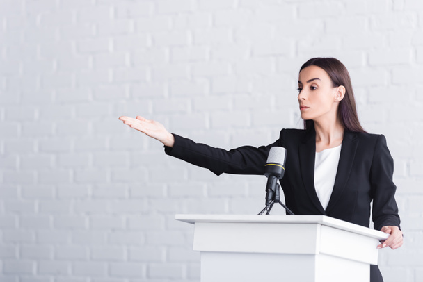 attractive, confident lecturer pointing with hand while standing on podium tribune - Foto, imagen