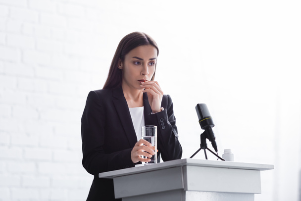 young lecturer suffering from speech anxiety standing on podium tribune with glass of water - Fotoğraf, Görsel