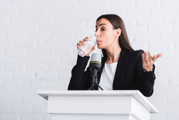 bonito, jovem palestrante beber água e gesticulando enquanto estava em tribuno pódio
 - Foto, Imagem