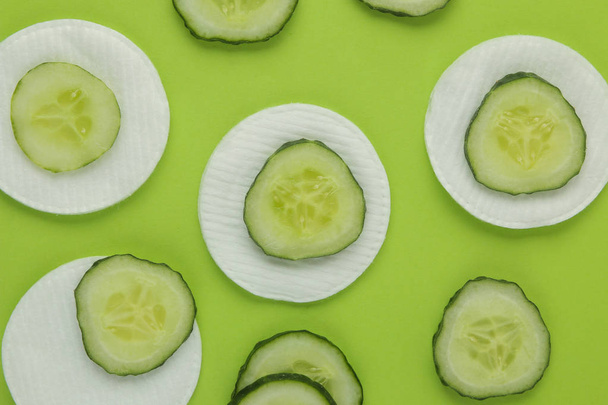 slices of fresh cucumber and cotton sponge on a bright green background. cucumber cosmetics concept. skin care. tonic cucumber extract - Foto, Imagem