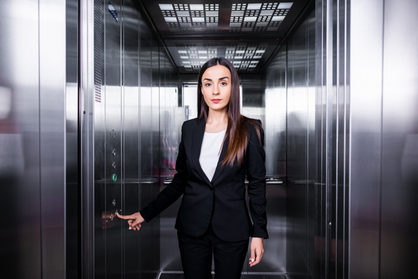 attrayant, confiant femme d'affaires en appuyant sur le bouton dans l'ascenseur et en regardant caméra
 - Photo, image