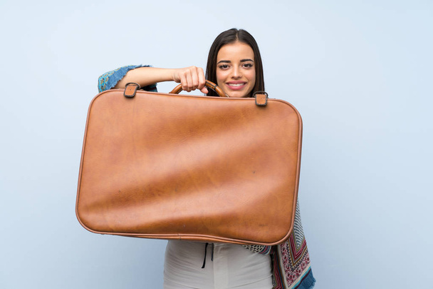 Young woman over isolated blue wall holding a vintage briefcase - Foto, Imagem