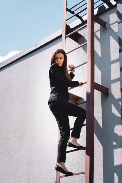 scared businesswoman looking down while climbing stairs on rooftop - Photo, Image