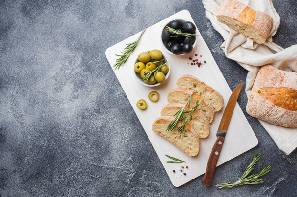 Italian ciabatta bread with olives and rosemary on a cutting Board. Dark concrete background. Copy space. - Фото, зображення