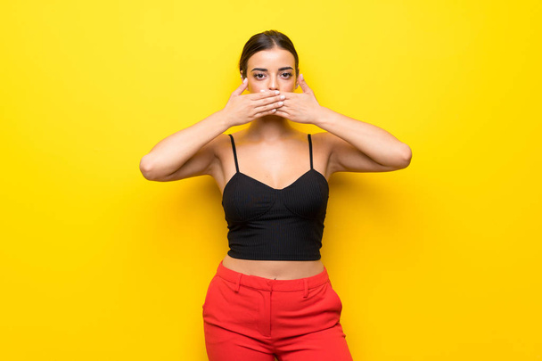 Young woman over isolated yellow background covering mouth with hands - Фото, зображення