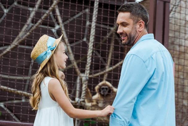 feliz padre mirando alegre y linda hija en sombrero de paja en zoológico
  - Foto, Imagen