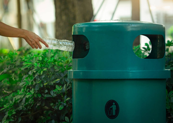 People hand throwing empty water bottle in recycle bin at park. Green plastic recycle bin. Man discard bottle in trash bin. Waste management. Plastic bottle garbage. Reduce and reuse plastic concept. - Photo, Image