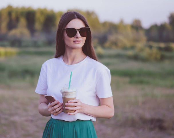 Девушка в солнечных очках летом держит кофейный коктейль
. - Фото, изображение