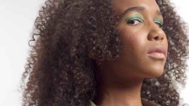 mladý smíšený model rasy ve studiu na bílém se kudrnatými vlasy, světle zelený oční make - Záběry, video