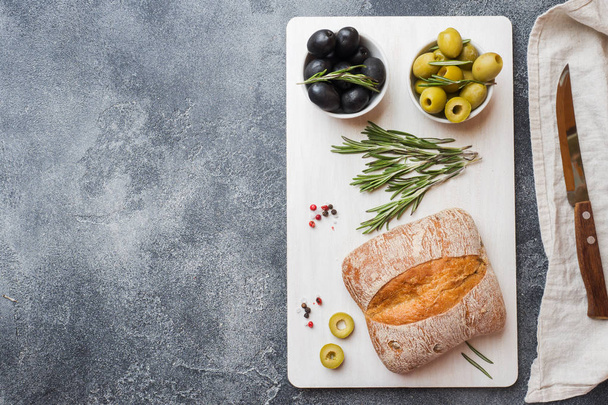 Italian ciabatta bread with olives and rosemary on a cutting Board. Dark concrete background. Copy space. - Fotó, kép