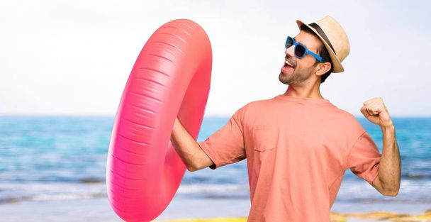 Man with hat and sunglasses on his summer vacation enjoy dancing while listening to music at a party at the beach - Photo, image