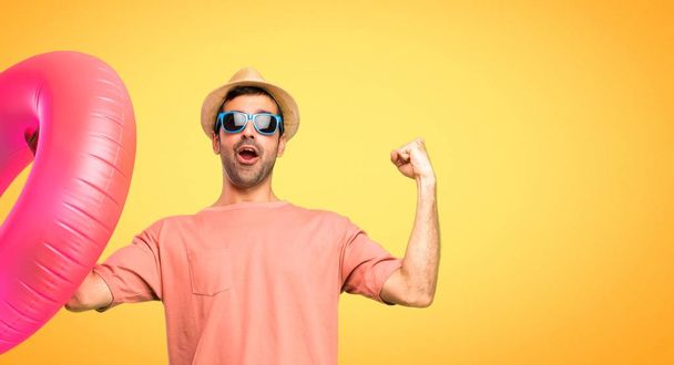 Man with hat and sunglasses on his summer vacation celebrating a victory in winner position on orange background - Fotó, kép