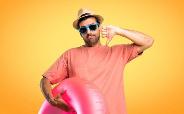 Férfi kalap és napszemüveg az ő nyári vakáció mutató hüvelykujját le mindkét kezével. Negatív kifejezés narancssárga háttérre - Fotó, kép