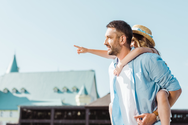 cheerful man piggybacking daughter pointing with finger near building  - Photo, image
