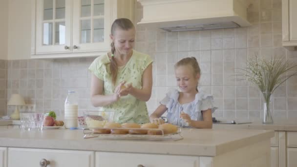 Pretty young mother and little cute daughter cook in the kitchen together. Real happy family. Relationship mom and daughter. Satisfied mom and girl give five and show thumbs up. - Filmati, video
