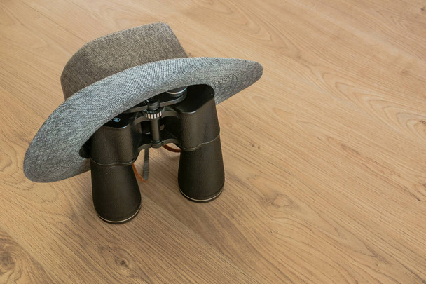 Wide-brimmed gray hat and binoculars, as symbols of travel. Wooden yellowish background. Preparation for the designer. Copy space. - Valokuva, kuva
