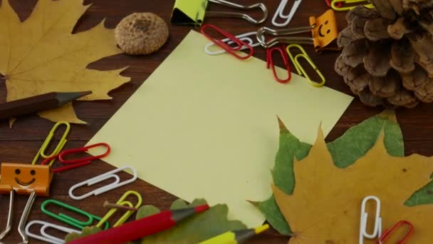 Κίτρινο φύλλο χαρτί με κίτρινα πεσμένα φύλλα σφενδάμου και αναλώσιμα γραφείου - Πλάνα, βίντεο
