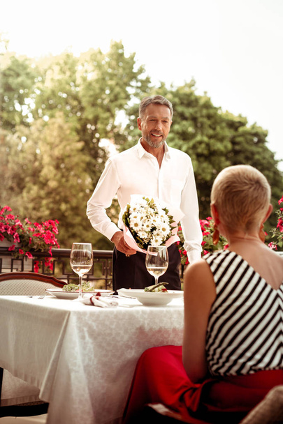 Husband bringing chamomiles for wife while having dinner outside - Zdjęcie, obraz