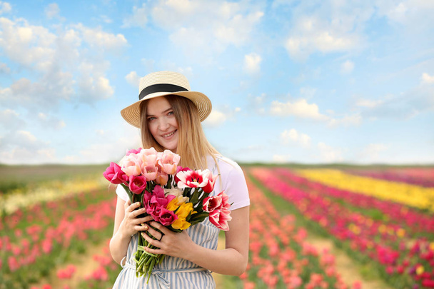 Beautiful young woman with bouquet of fresh tulips in countryside on spring day - Photo, Image