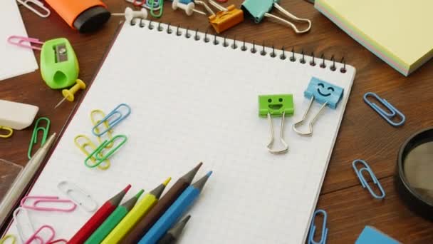 Χαμόγελα μπλε και πράσινο ντοσιέ κλιπ στο σημειωματάριο με πολύχρωμα μολύβια και κλιπ χαρτιού - Πλάνα, βίντεο