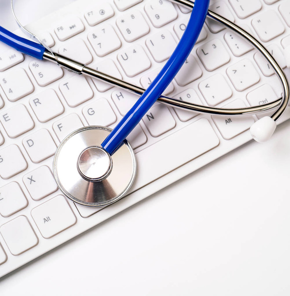 白いテーブルの背景にコンピュータのキーボード上の青い聴診器。オンライン医療情報治療技術コンセプト、クローズアップ、マクロ、コピースペース - 写真・画像