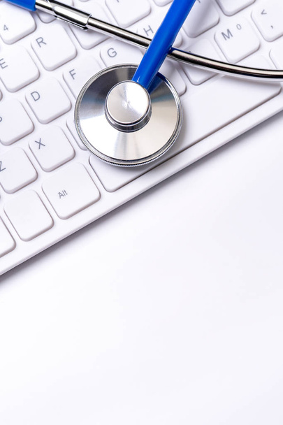 Beyaz masa arka planı üzerinde bilgisayar klavyesi üzerinde Mavi stetoskop. Online tıbbi bilgi tedavi teknolojisi kavramı, yakın çekim, makro, kopyalama alanı - Fotoğraf, Görsel