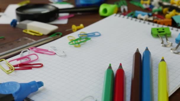 Vícebarevné tužky, kancelářské sponky a notebook na hnědém dřevěném stole - Záběry, video