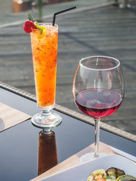 テーブルの上に赤ワインのグラスと熱帯オレンジカクテル - 写真・画像