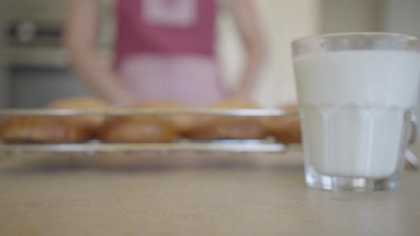 Two glasses of milk on the table on the background a young woman and freshly baked buns from the oven. Close up. Advertising concept - Imágenes, Vídeo