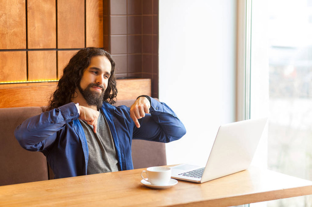 boze knappe jonge leider man freelancer in casual stijl zittend in café en praten in laptop terwijl het tonen van vingers naar beneden  - Foto, afbeelding
