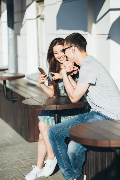 Молодая пара подростков друзья одеты в случайный стиль сидя вместе и с помощью мобильного на улице города
 - Фото, изображение