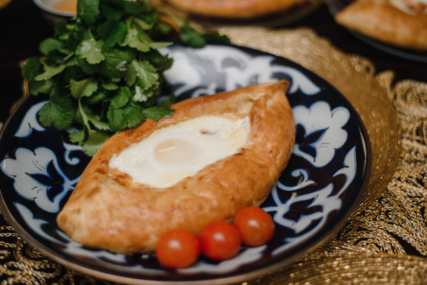 Ο Αζαρά κατσούρι στο ανατολικό τραπέζι. αυγό σε ζεστό ψωμί σε ανατολίτικες πλάκες είναι σε ένα εστιατόριο. - Φωτογραφία, εικόνα
