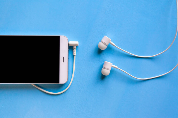 smartphone branco com fones de ouvido brancos conectados no fundo azul
 - Foto, Imagem