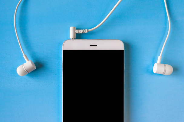 smartphone branco com fones de ouvido brancos conectados no fundo azul
 - Foto, Imagem
