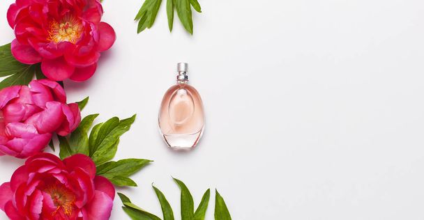 Parfümös üveg és rózsaszín virágok pünkösdi rózsa a világosszürke háttér felülnézet lapos feküdt másolási hely. Illatszerek, kozmetikumok, női kiegészítők, illatanyag-gyűjtemény. Finom Pink parfümös üveg - Fotó, kép