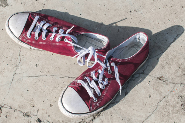 Pair of worn out vintage red old canvas sneakers on outside concrete surface - Photo, Image